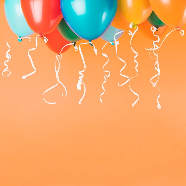 Photo colorful balloons with ribbons on orange background with copy space
