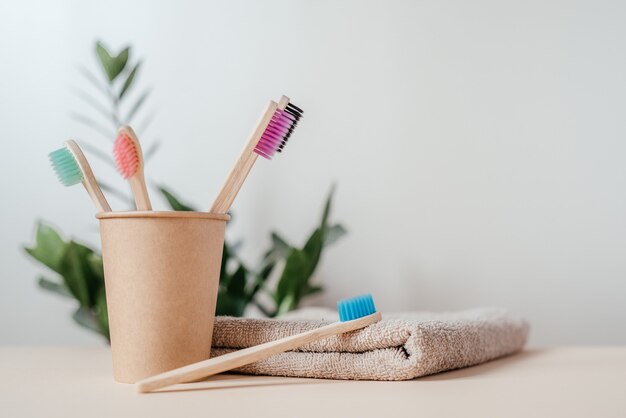 Colorful bamboo toothbrushes in a paper cup with a towel and green plant dental care with zero waste concept sustainable lifestyle