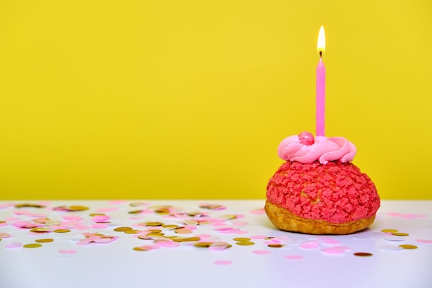 A colorful birthday cupcake with one candle and confetti on a yellow background