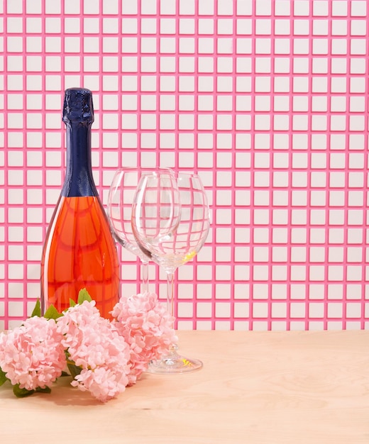 A colorful bottle of holiday champagne two glasses and spring's beautiful fresh pink flowers Copy space for text Atmosphere of romance and pleasant experiences