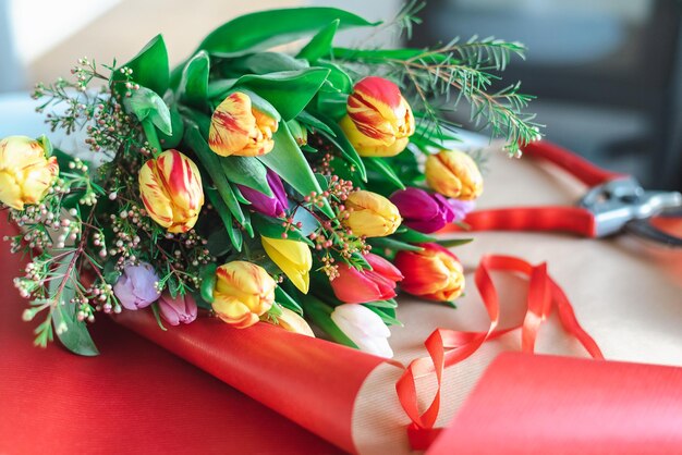 A colorful bouquet of spring tulips lies on a bright red wrapping paper