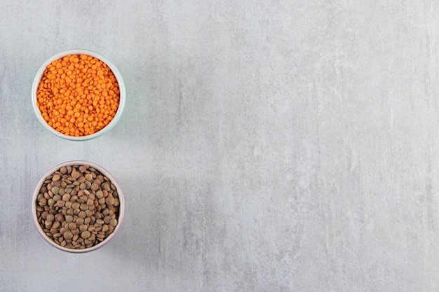 Colorful bowls with raw lentil and buckwheat on stone background. 