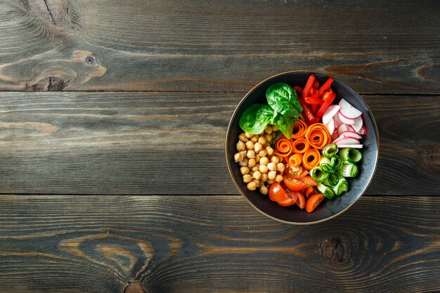 Colorful Buddha Bowl with chickpeas, carrots, tomatoes, cucumbers, radish and peppers on wooden table. Vegetarian salad. Top view. Copy space.