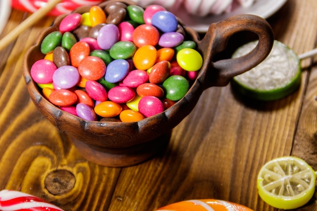 Colorful button shaped candies filled with chocolate in ceramic bowl on wooden table