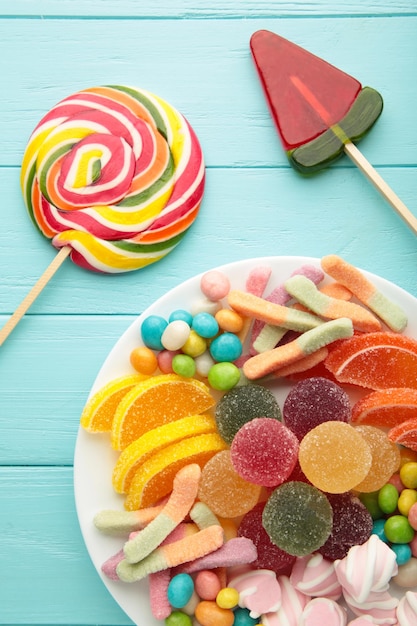 Colorful candies lollipops and jelly in plate on blue wooden background.