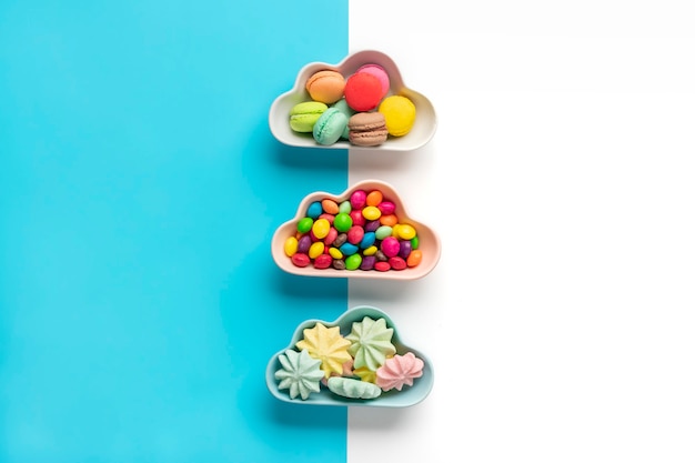 colorful candies - lollipops, meringues, macaroon in bowl in shape of cloud isolated on blue, white