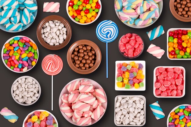 colorful candies marshmellows chocolate balls in jars lollipops and sweet peanuts in dark background