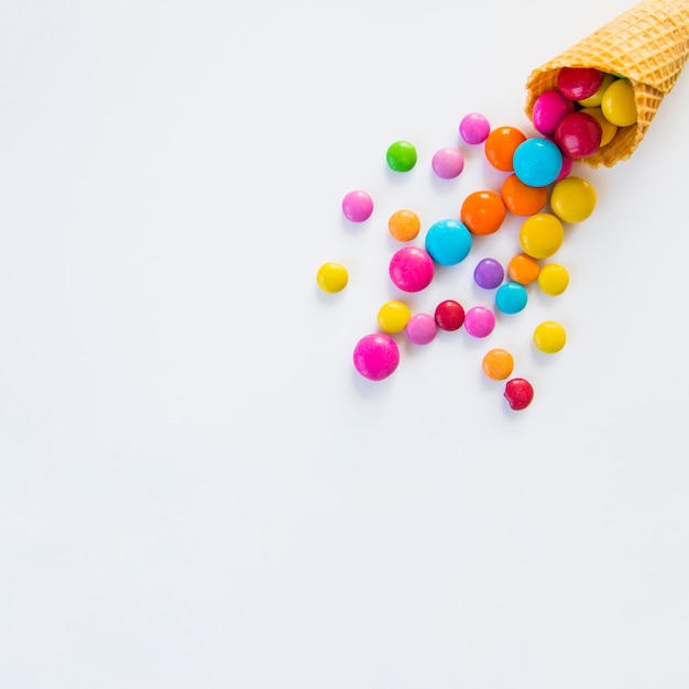 Colorful candies spilled from a waffle cone on white background