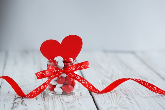 赤い弓と赤い紙のハートで飾られたカラフルなキャンディーの瓶。バレンタインデーのコンセプト