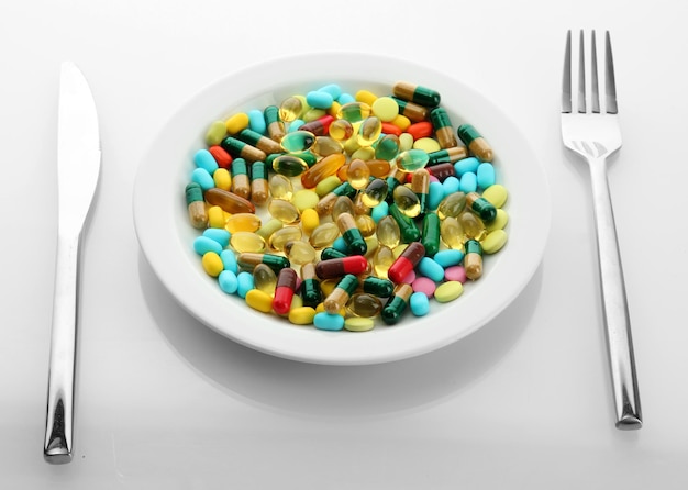 Colorful capsules and pills on plate with fork and knife isolated on white