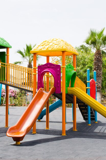 Colorful children playground activities in public park surrounded by green trees.