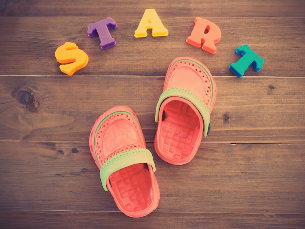 Colorful children's rubber sandals and colorful alphabets START word on wooden floor