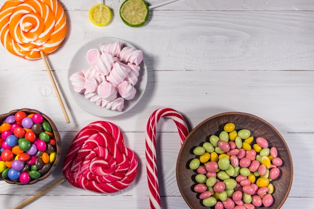 Colorful chocolate candies lollipops candy cane and marshmallows on white wooden table