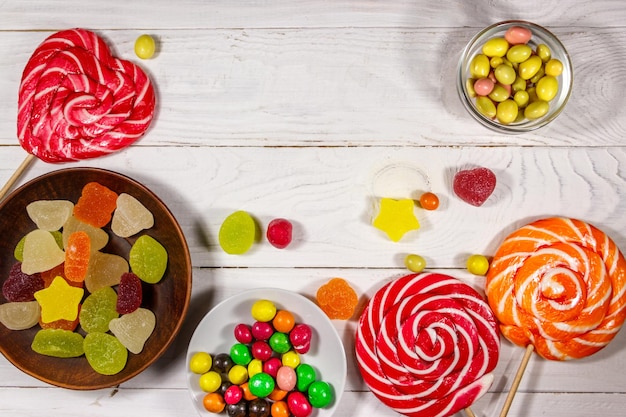 Colorful chocolate candies, lollipops and jelly sweets on white wooden table