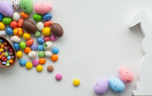 Красочные и шоколадные пасхальные яйца со сладким драже на белом фоне