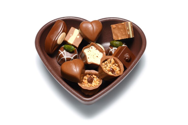Photo colorful chocolates in a heartshaped bowl on a white background
