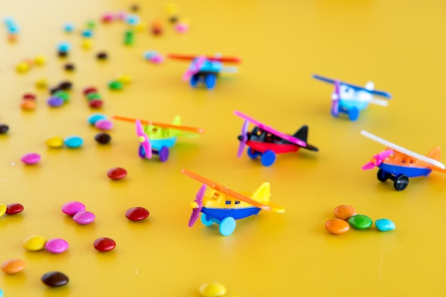 Colorful chocolates and plastic toys on a yellow background