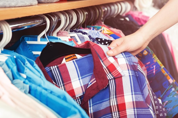 Colorful clothes hanging on a hanger and a female hand holding a shirt