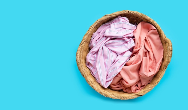 Colorful clothes in laundry basket on blue background. Copy space