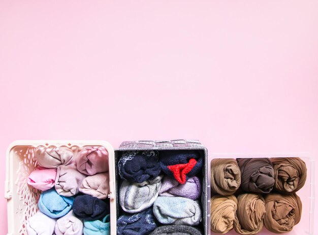 Colorful clothes vertical storage in home wardrobe. Items of clothing in plastic and textile box on soft pink background.