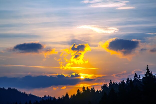 山岳地帯の森林地帯を背景に夕暮れ時の空に色とりどりの雲