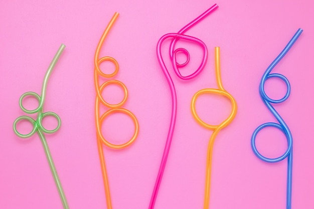 Colorful cocktail straws on pink paper background.