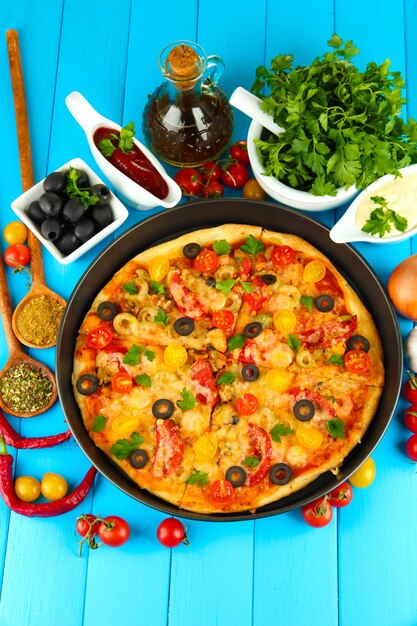 Colorful composition of delicious pizza vegetables and spices on blue wooden background closeup