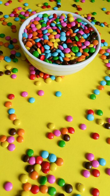 Colorful confetti scattered on yellow table, top view.