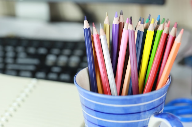 Colorful crayon in the blue cup on work table.