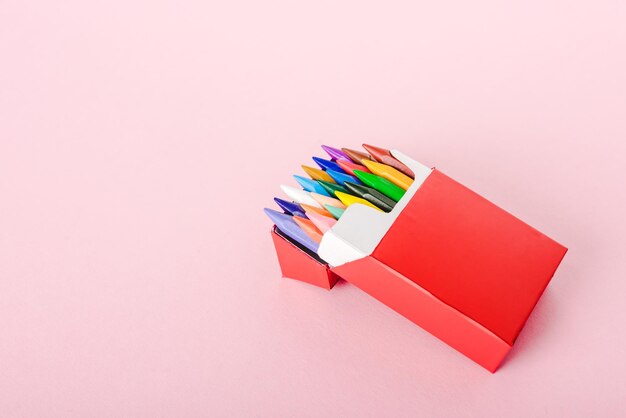 Colorful crayons in cigarette pack on pink with copy space smoking concept