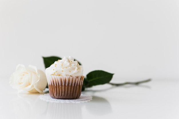 Colorful cupcake on doily with rose against white background