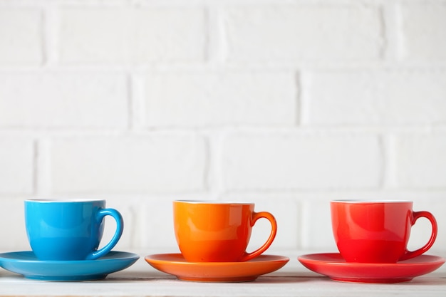 Colorful cups on the white background of a brick wall. Background with copy space. Horizontal. Selective focus.