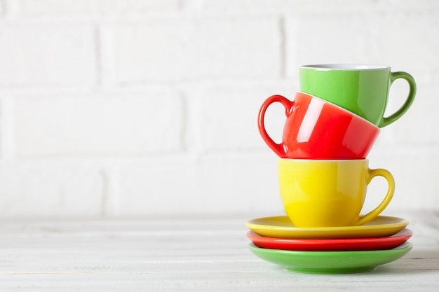 Colorful cups on the white background of a brick wall. Background with copy space. Horizontal. Selective focus.