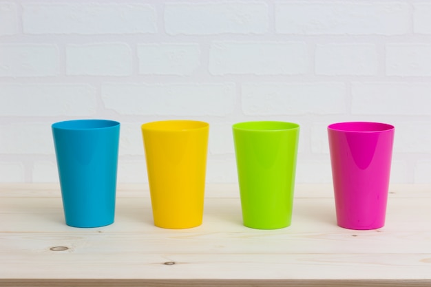 Colorful cups on wooden table white brick wall.