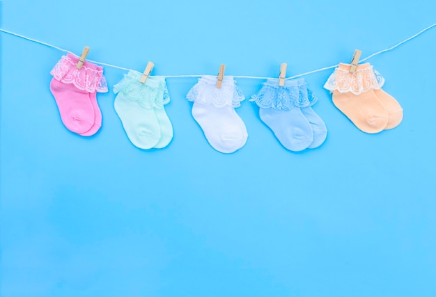 Colorful cute baby socks hanging on the clothesline on blue background. Baby accessories. Flat lay.