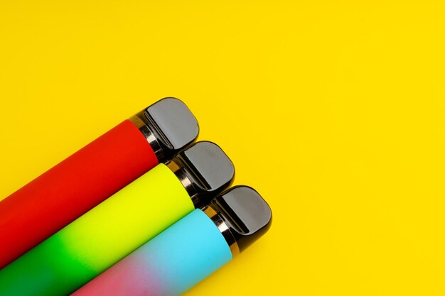 Colorful disposable electronic cigarettes on yellow background