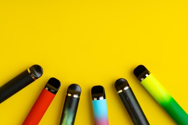 Colorful disposable electronic cigarettes on yellow background