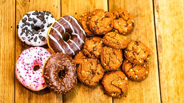 Colorful donuts and biscuits on wooden table Sweet icing sugar food with glazed sprinkles doughnut with chocolate frosting Top view with copy space