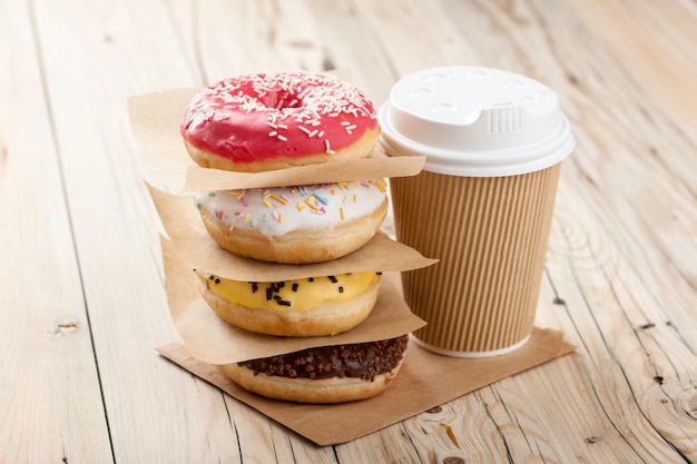 Colorful donuts and paper cup on wooden table, close up