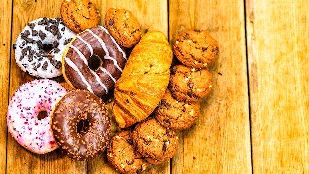 Colorful donuts puff pastry and biscuits on wooden table sweet icing sugar food with glazed sprinkles doughnut with chocolate frosting top view with copy space