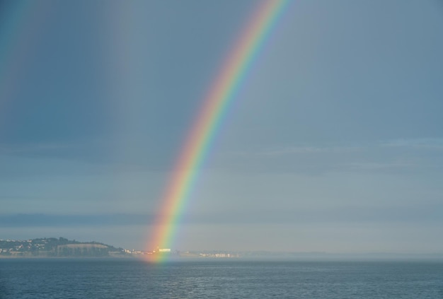 Красочная и драматичная двойная радуга формируется у береговой линии и видна с корабля в океане.