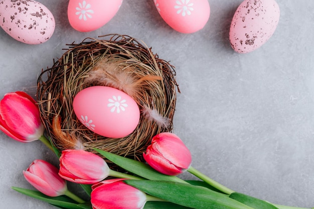 Colorful Easter egg in the nest with tulip flowers on gray stone concrete background top view copy space Happy Easter holidays