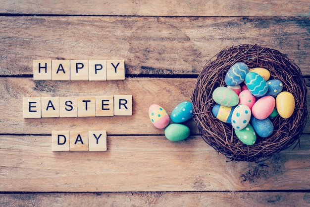 Colorful easter egg in the nest and wood text for Happy Easter Day on wood background with space