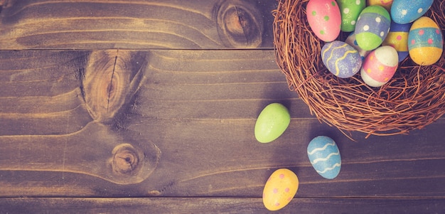 Colorful easter egg and nest on wooden background with space.