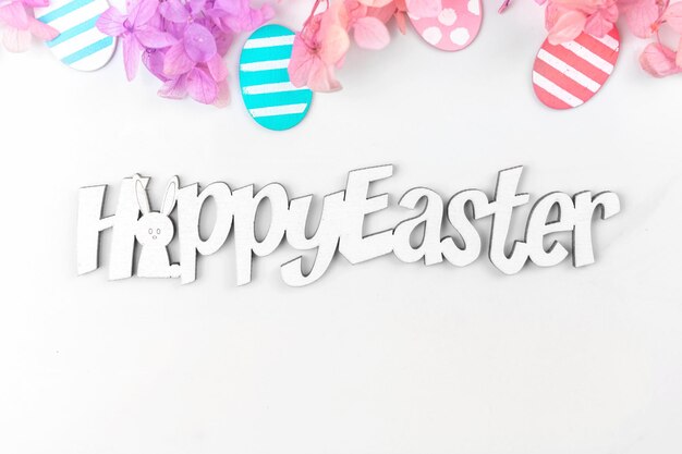 Colorful easter eggs and flowers Border design with pink spring flowers Happy easter text greetings concept holiday decoration background with copy space flat lay top view photo