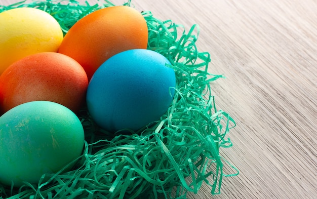 Foto uova di pasqua colorate nel nido verde sul legno bianco.