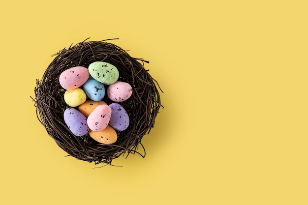 Colorful Easter eggs inside a nest on yellow background Copy space