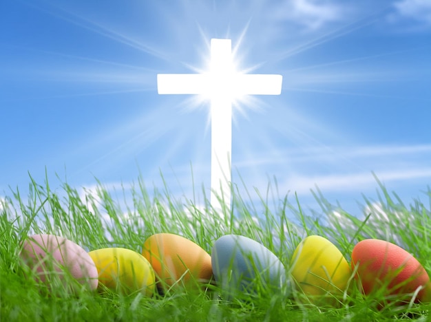 Colorful easter eggs laying on the grass and a bright cross on\
a background