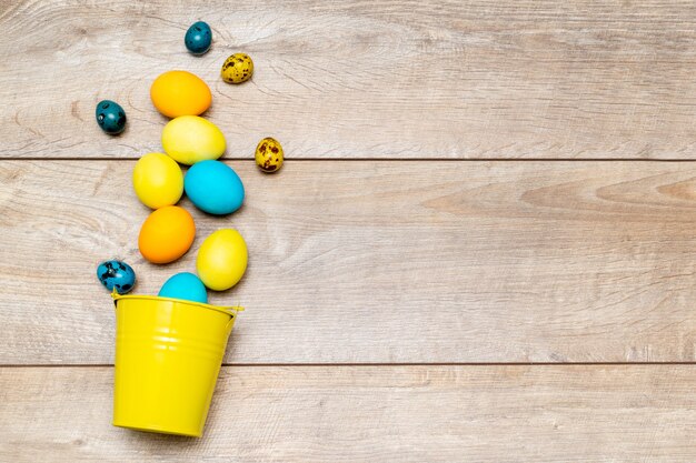 Colorful easter eggs lie in decor bucket on wooden surface