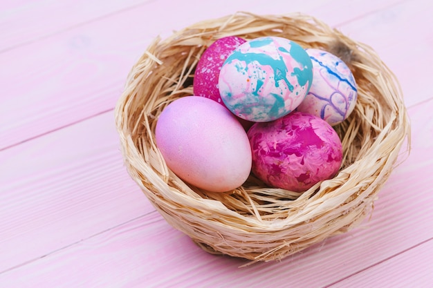 Colorful easter eggs in a nest on pink wooden surface 